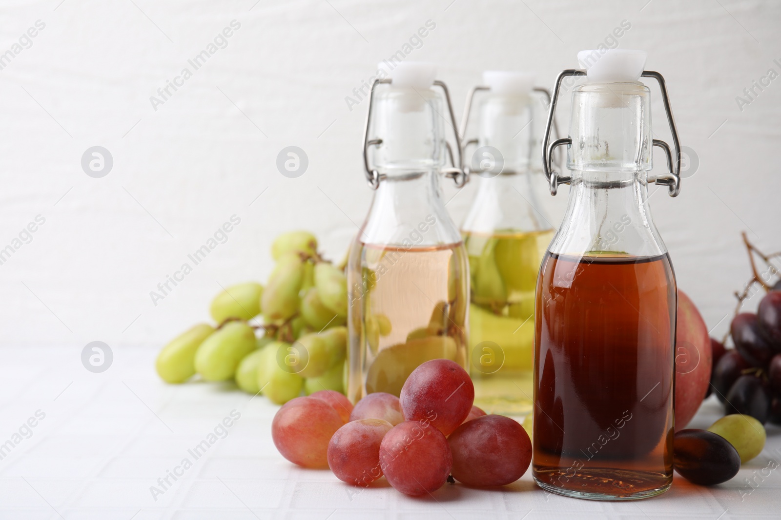 Photo of Different types of vinegar and ingredients on light tiled table, closeup. Space for text