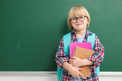 Happy little school child with notebooks near chalkboard. Space for text