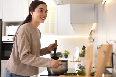Photo of Smiling woman with ladle cooking soup in kitchen