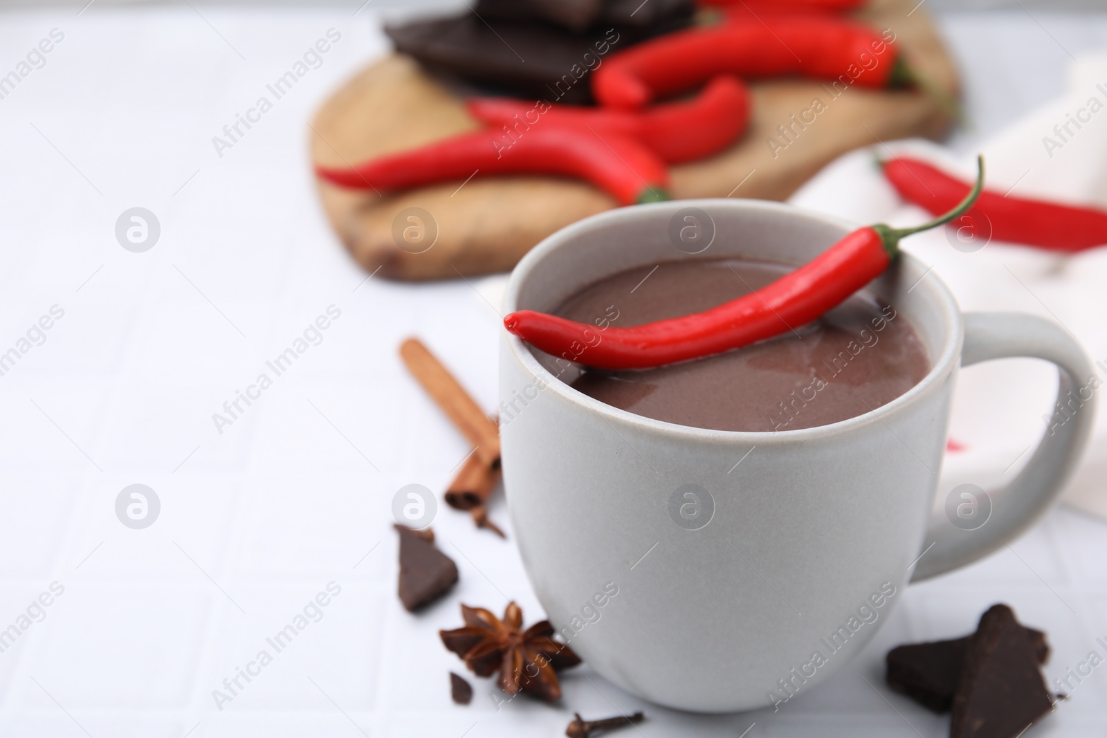 Photo of Cup of hot chocolate with chili pepper on white tiled table. Space for text