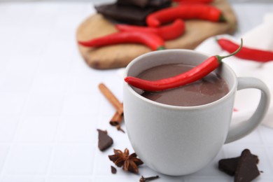 Photo of Cup of hot chocolate with chili pepper on white tiled table. Space for text