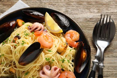 Photo of Delicious spaghetti with seafood served on wooden table, flat lay