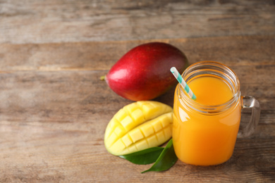 Photo of Mason jar of delicious mango drink on wooden table. Space for text