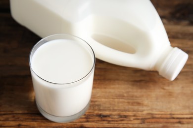 Photo of Glass of milk near gallon bottle on wooden table, closeup