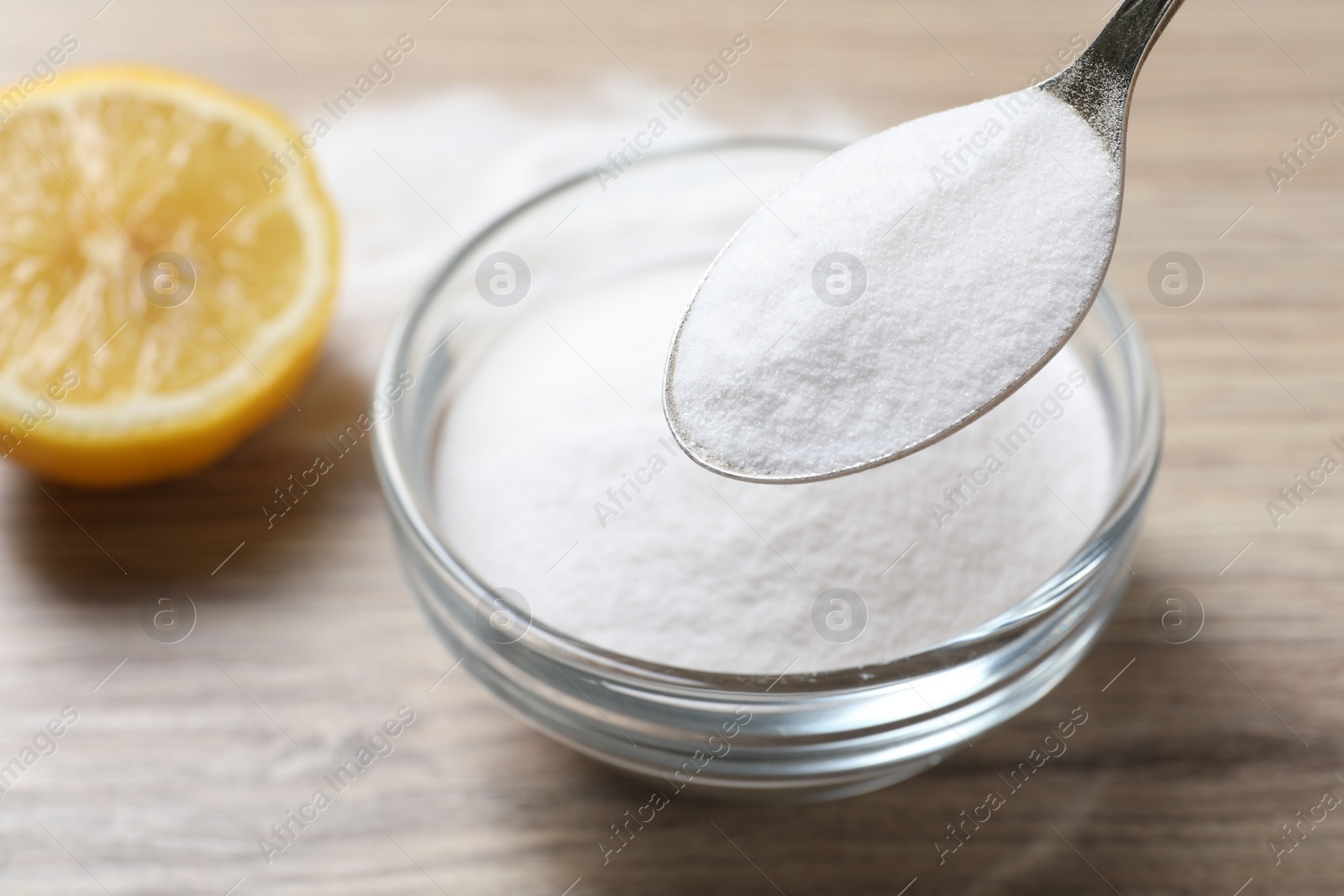 Photo of Taking baking soda from bowl at wooden table, closeup