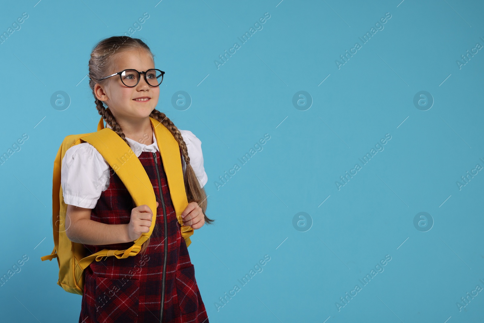Photo of Happy schoolgirl in glasses with backpack on light blue background, space for text