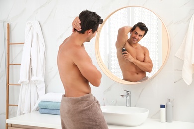 Handsome young man applying deodorant in bathroom