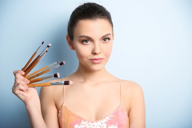 Young woman with makeup brushes on color background. Professional cosmetic products