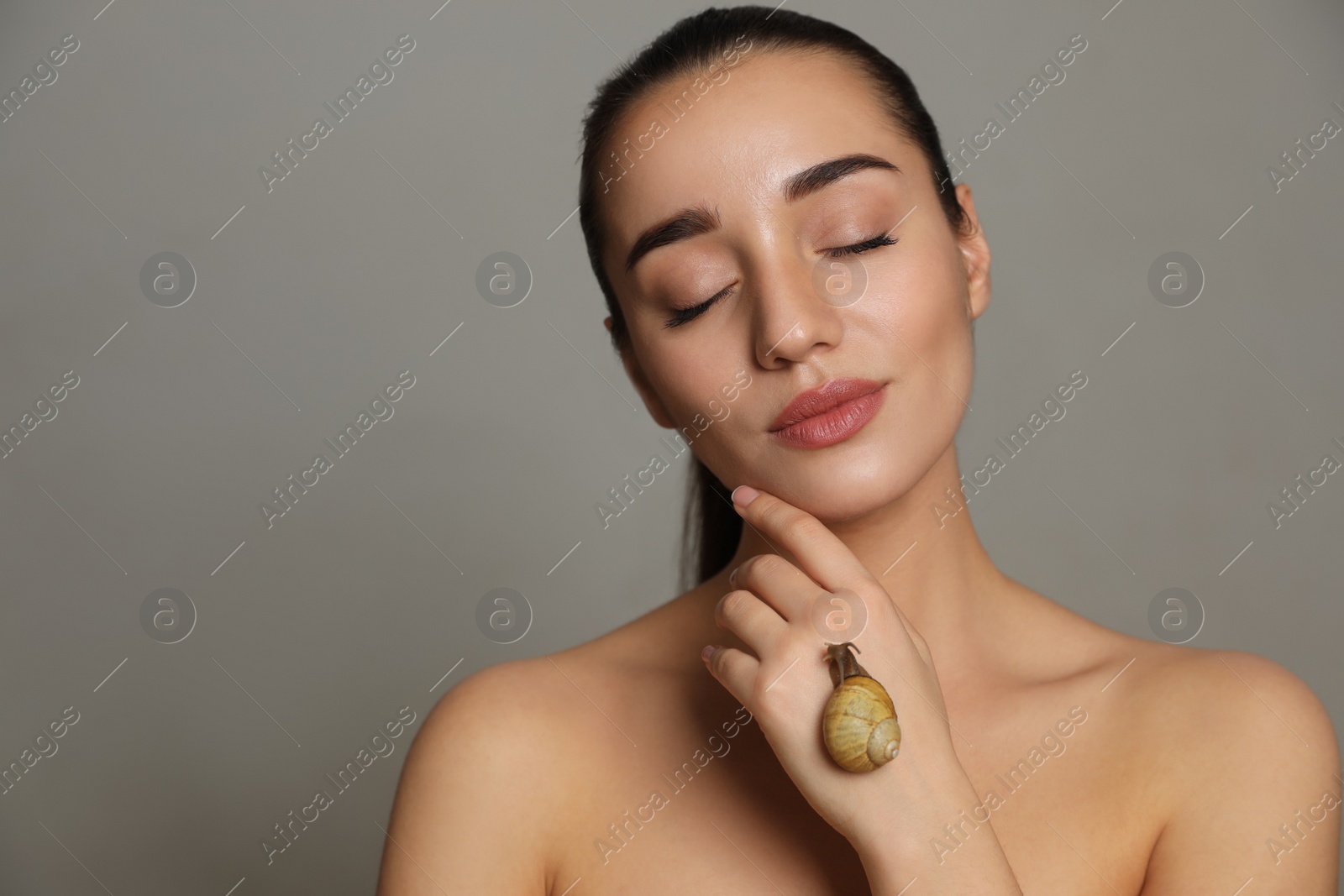 Photo of Beautiful young woman with snail on her hand against grey background. Space for text