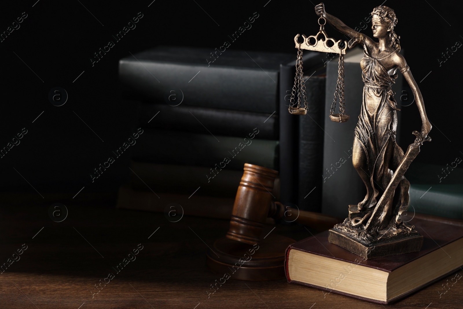 Photo of Symbol of fair treatment under law. Statue of Lady Justice near books and gavel on wooden table, space for text.