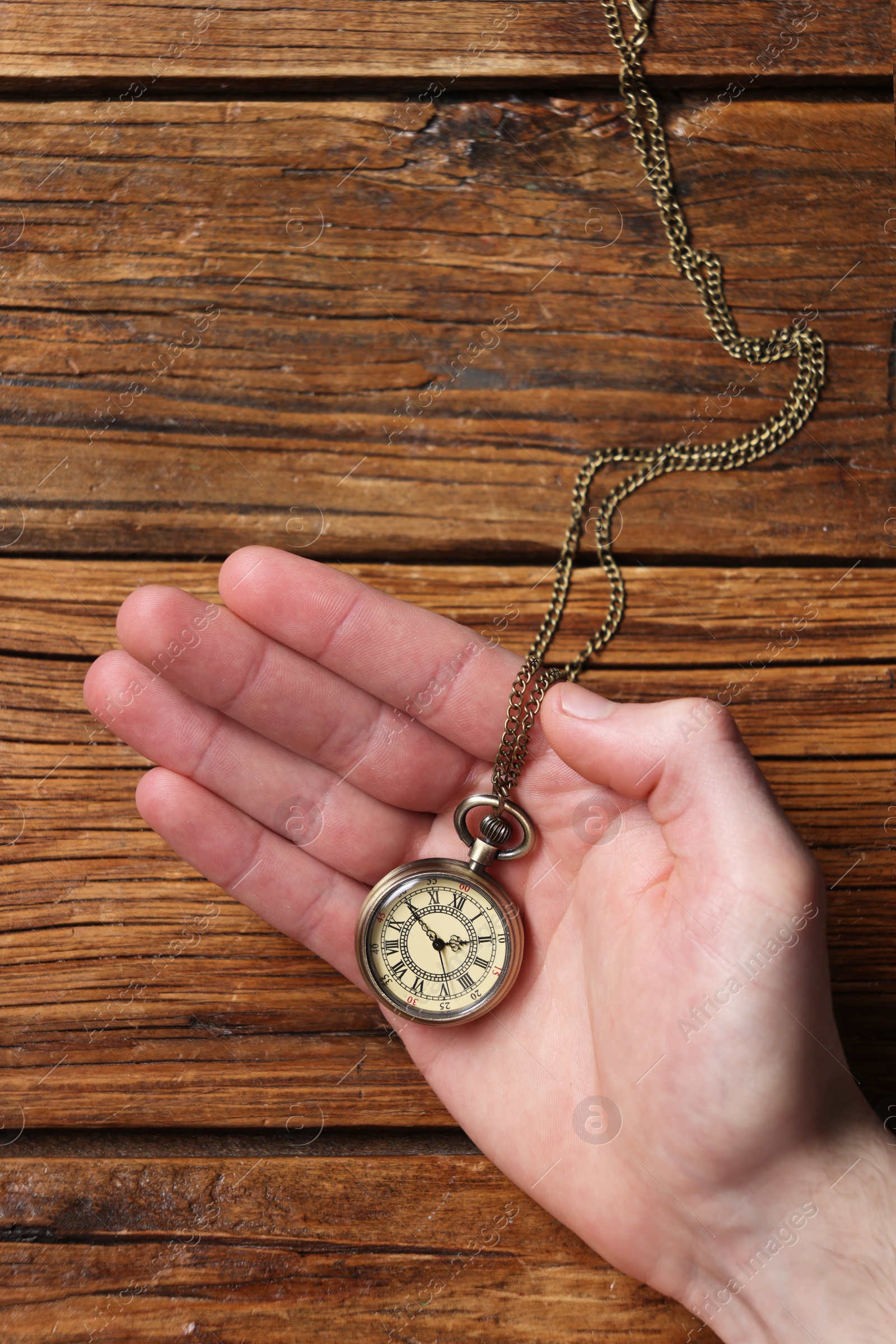 Photo of Man holding chain with elegant pocket watch at wooden table, top view
