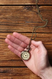 Man holding chain with elegant pocket watch at wooden table, top view