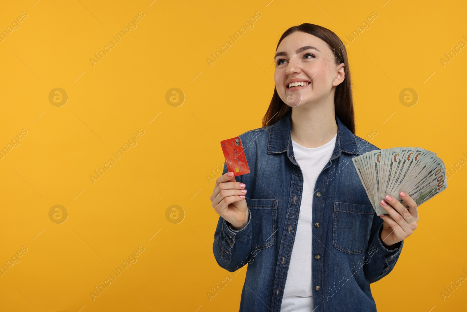 Photo of Happy woman with credit card and dollar banknotes on orange background, space for text