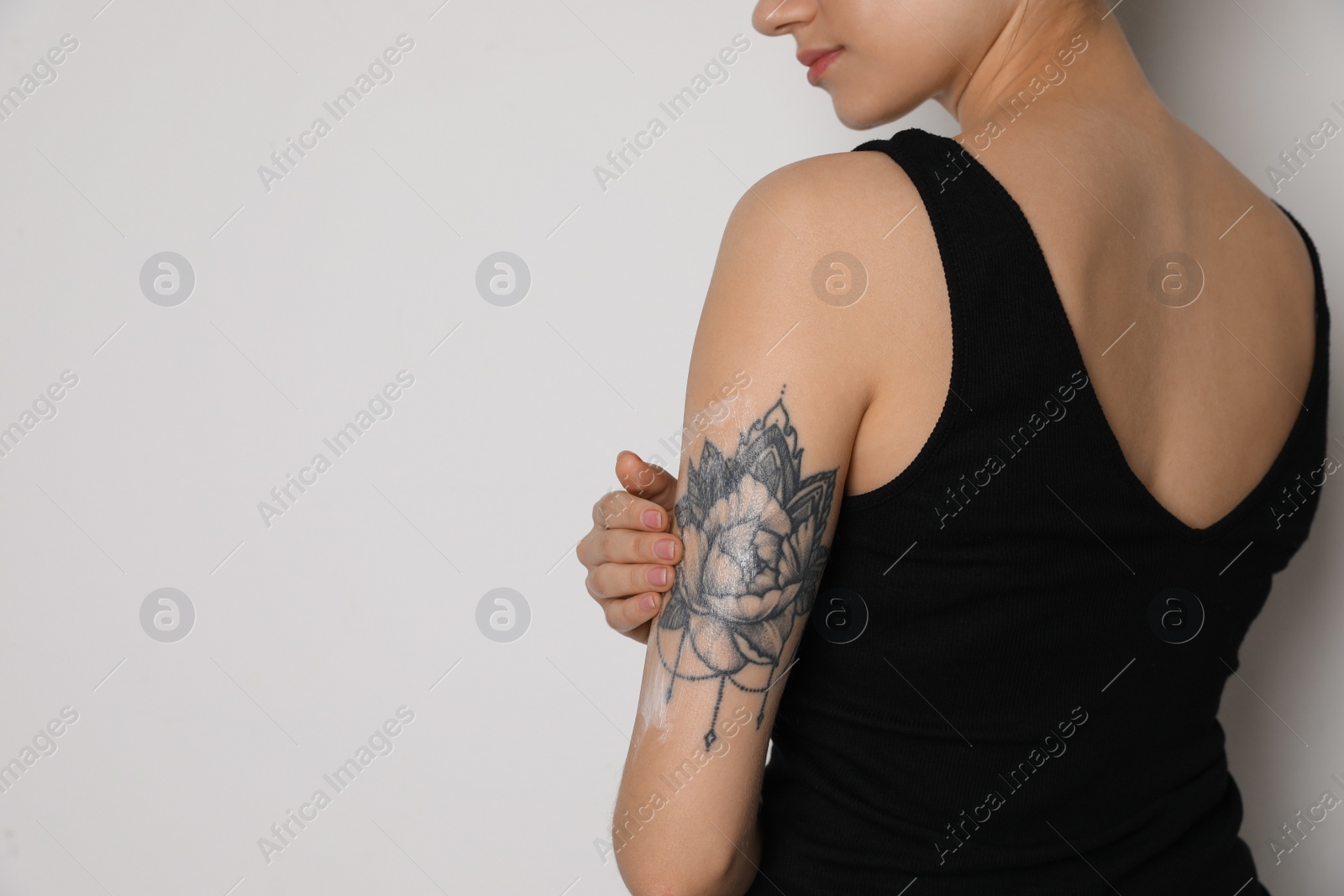 Photo of Woman applying cream onto her arm with tattoo on white background, closeup. Space for text