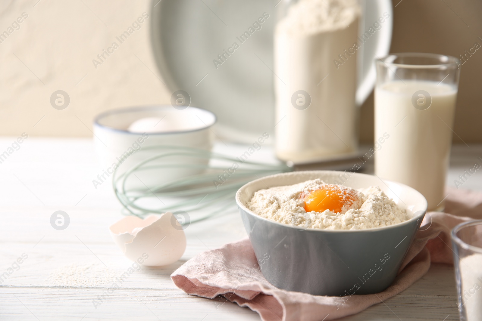 Photo of Making dough. Flour with yolk in bowl on white wooden table, closeup