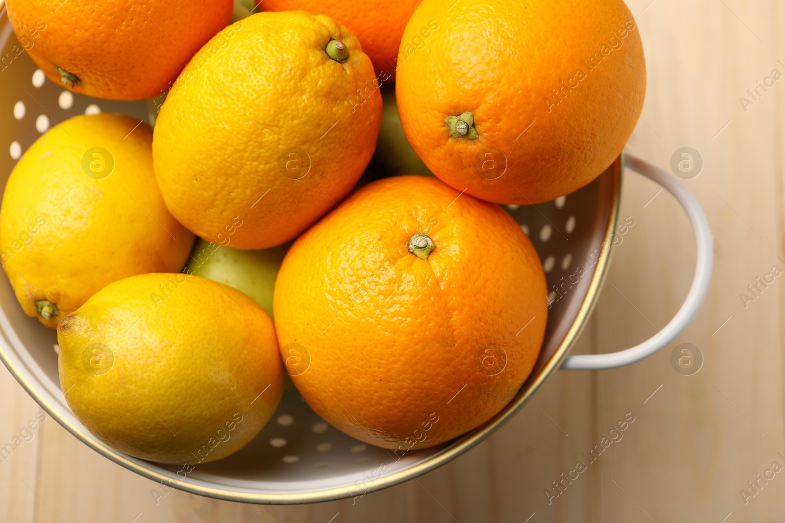 Photo of Colander with fresh citrus fruits on wooden table, top view