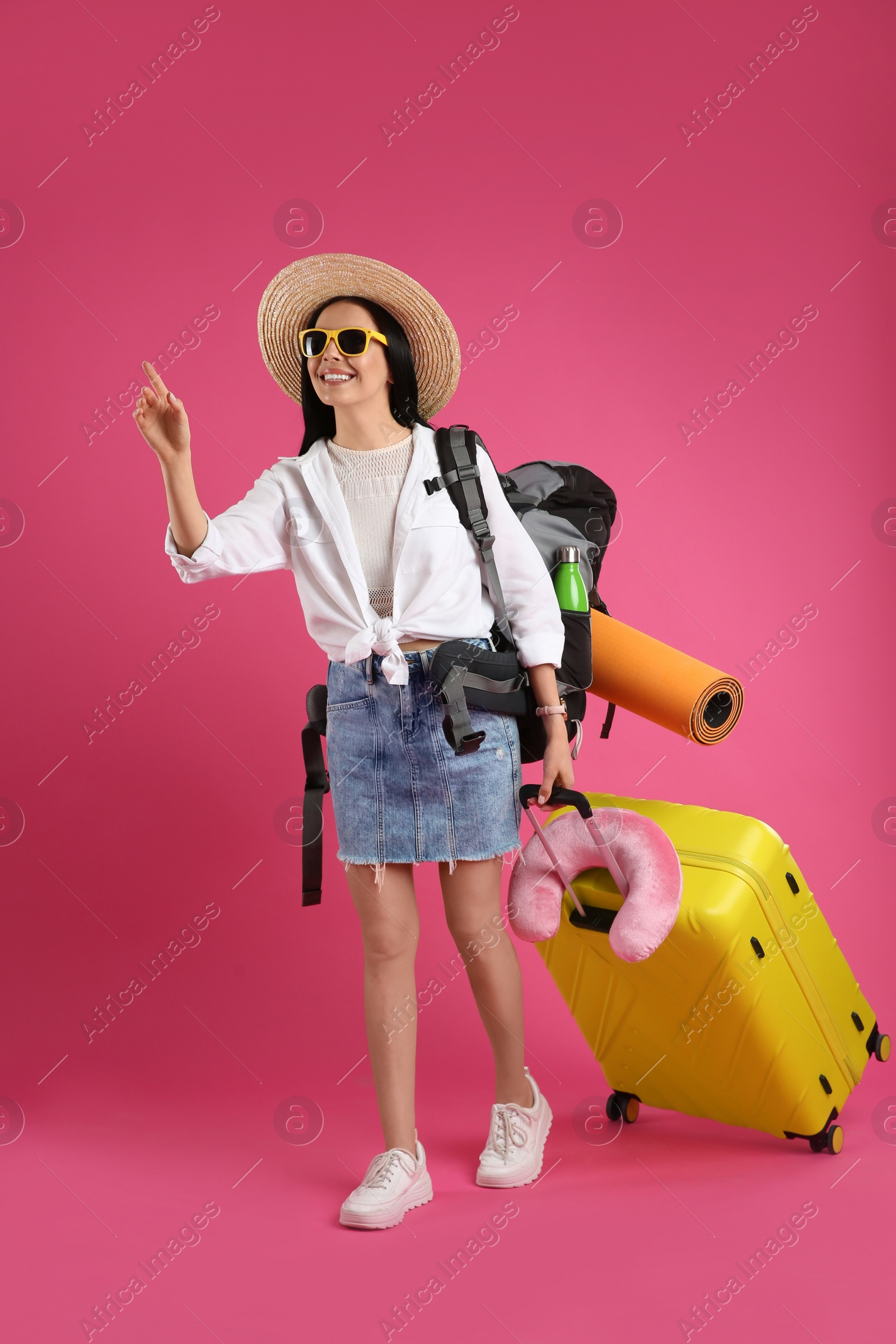 Photo of Female tourist with backpack, suitcase and travel pillow on pink background