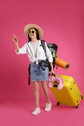 Female tourist with backpack, suitcase and travel pillow on pink background