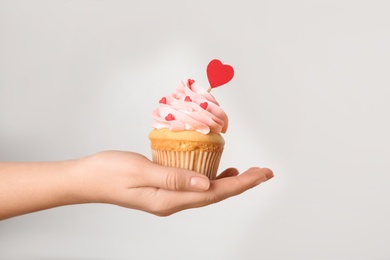 Woman holding tasty cupcake for Valentine's Day on light background, closeup
