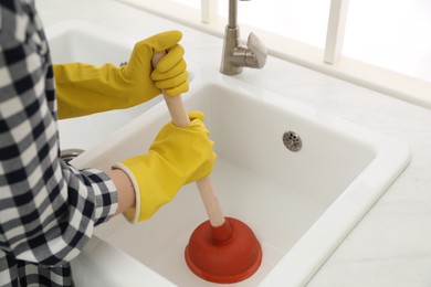 Photo of Woman using plunger to unclog sink drain in kitchen, closeup