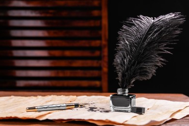 Photo of Inkwell with lush feather, fountain pen and vintage parchment with ink stains on wooden table indoors. Space for text