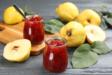 Photo of Delicious quince jam and fruits on grey wooden table