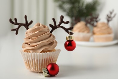 Tasty cupcake with chocolate reindeer antlers and Christmas bauble on white table. Space for text