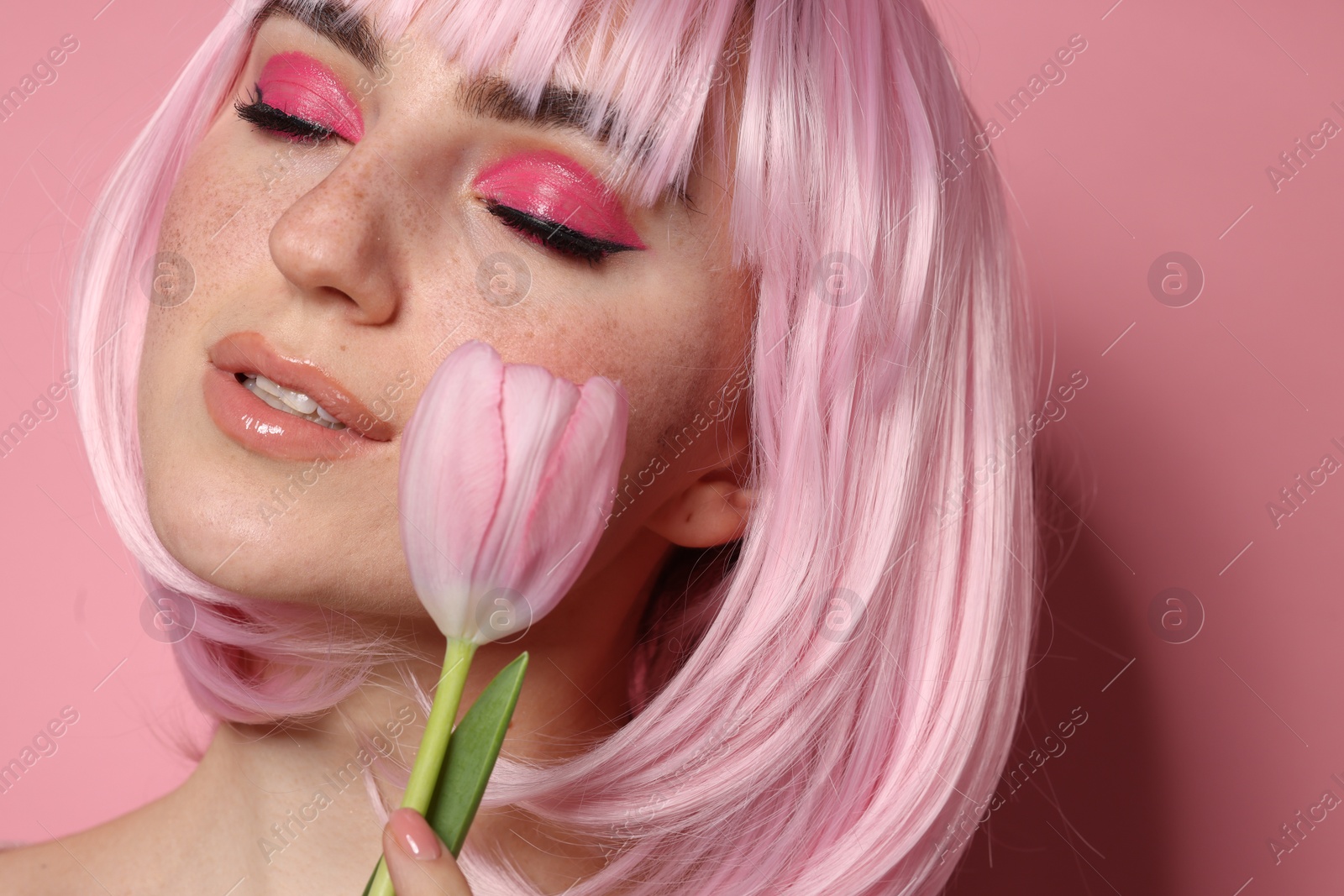 Photo of Beautiful woman with bright makeup, fake freckles and tulip on pink background, closeup