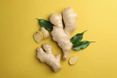 Photo of Fresh ginger with green leaves on pale light yellow background, flat lay