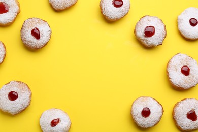 Frame of Hanukkah donuts with jelly and powdered sugar on yellow background, flat lay. Space for text