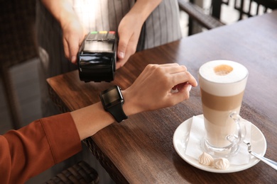 Woman making payment with smart watch in cafe, closeup