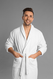 Happy young man in bathrobe on grey background