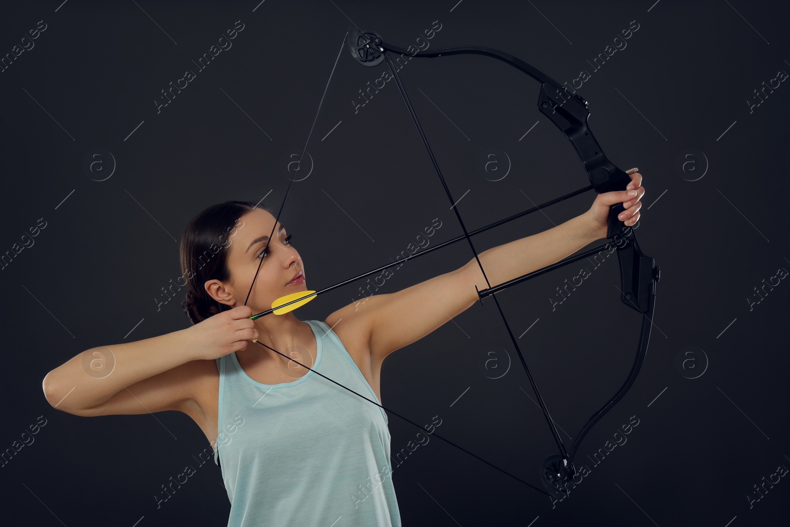 Photo of Sporty young woman practicing archery on black background