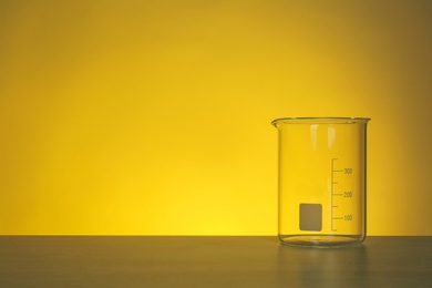 Photo of Empty beaker on table against color background. Chemistry laboratory glassware