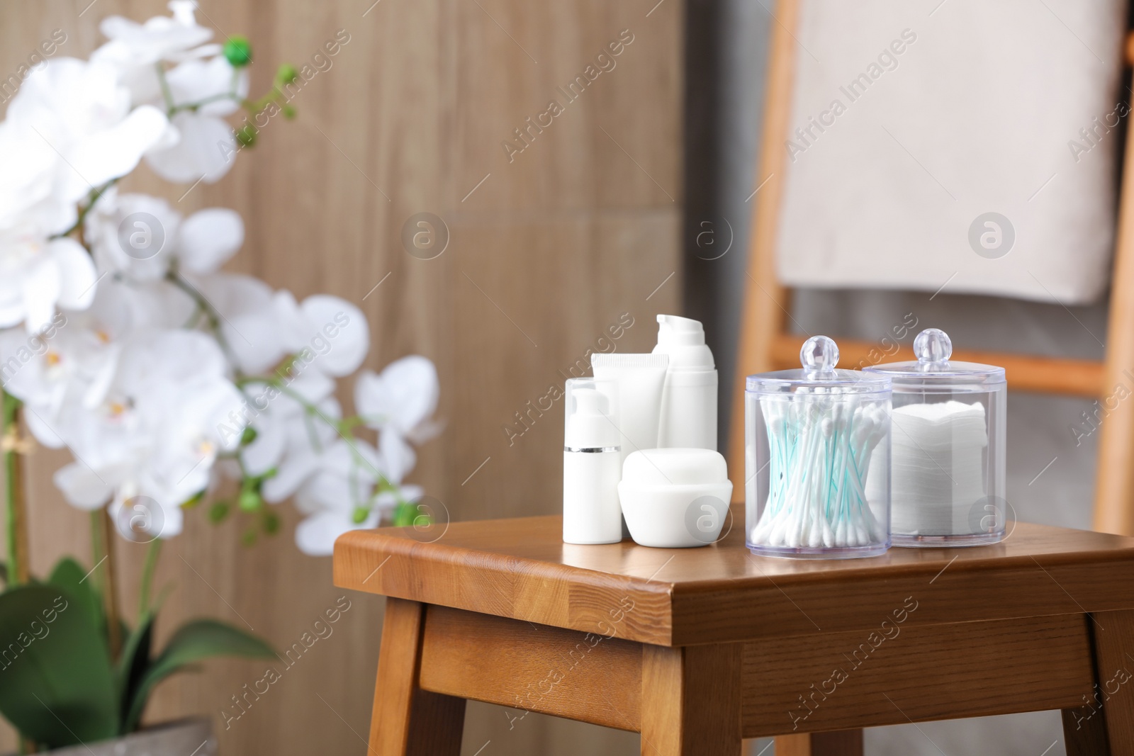 Photo of Cotton pads and swabs near cosmetic products on wooden stool in room. Space for text