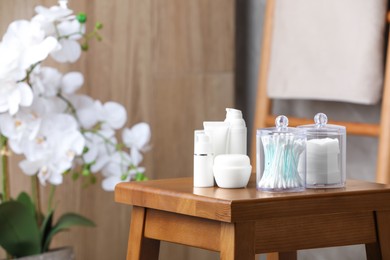 Cotton pads and swabs near cosmetic products on wooden stool in room. Space for text