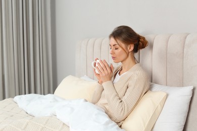 Beautiful woman with cup of drink in bed at home