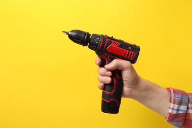 Handyman holding electric screwdriver on yellow background, closeup