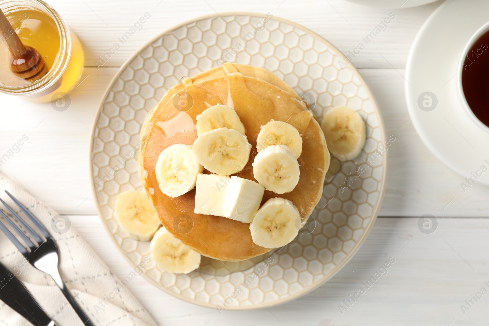 Photo of Delicious pancakes with bananas, honey and butter served on white wooden table, flat lay