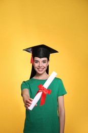 Photo of Happy student with graduation hat and diploma on yellow background