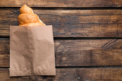 Photo of Tasty fresh croissant in paper bag on wooden table, top view. Space for text