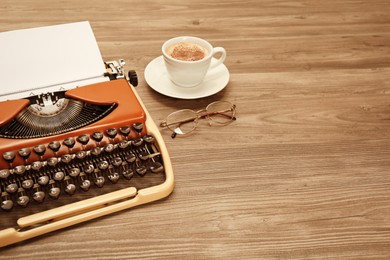 Vintage typewriter, glasses and cup of coffee on wooden table. Space for text