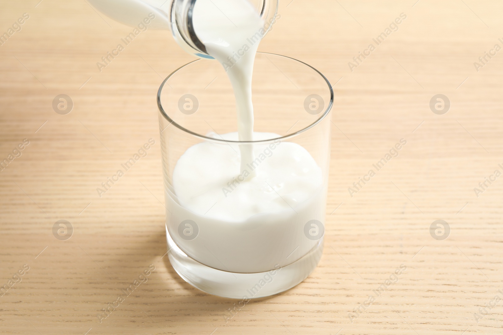 Photo of Pouring milk into glass on wooden table