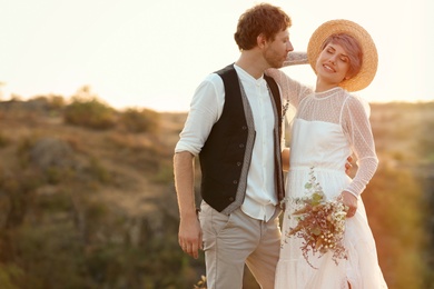 Photo of Happy newlyweds with beautiful field bouquet outdoors