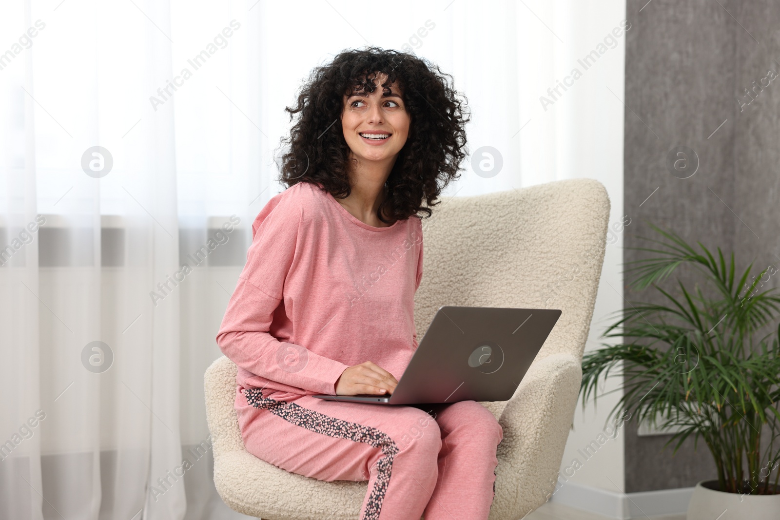 Photo of Beautiful young woman in stylish pyjama with laptop on armchair at home
