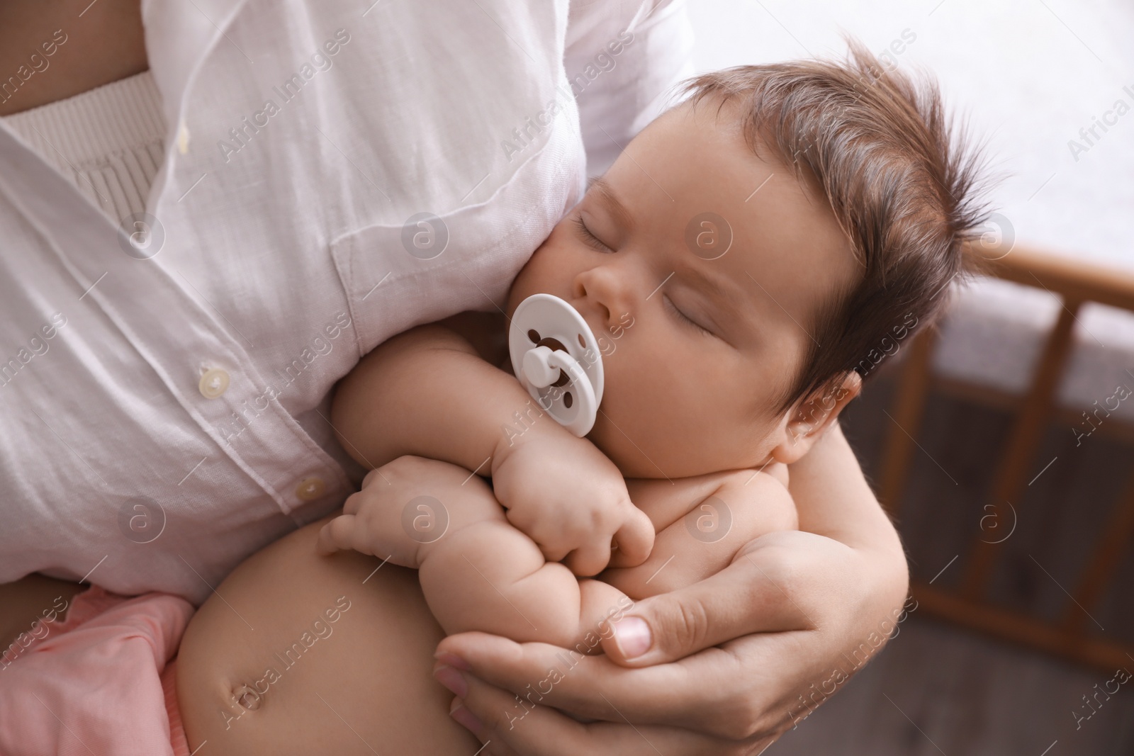 Photo of Mother holding her cute sleeping baby with pacifier at home, closeup