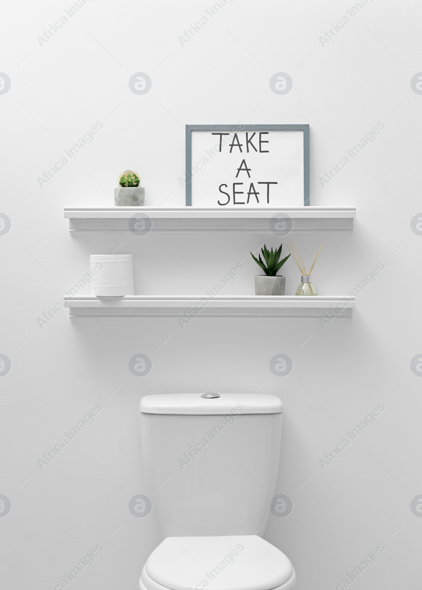 Photo of Toilet bowl, decor elements and funny sign near white wall. Bathroom interior