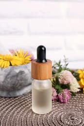 Photo of Glass bottle of essential oil, mortar with pestle and different wildflowers on wicker mat
