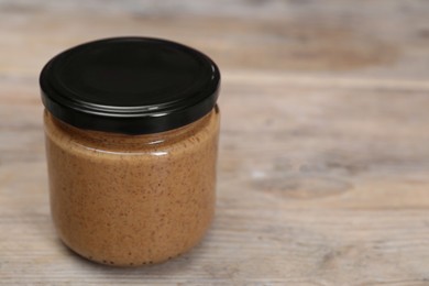 Tasty nut paste in jar on wooden table, closeup. Space for text