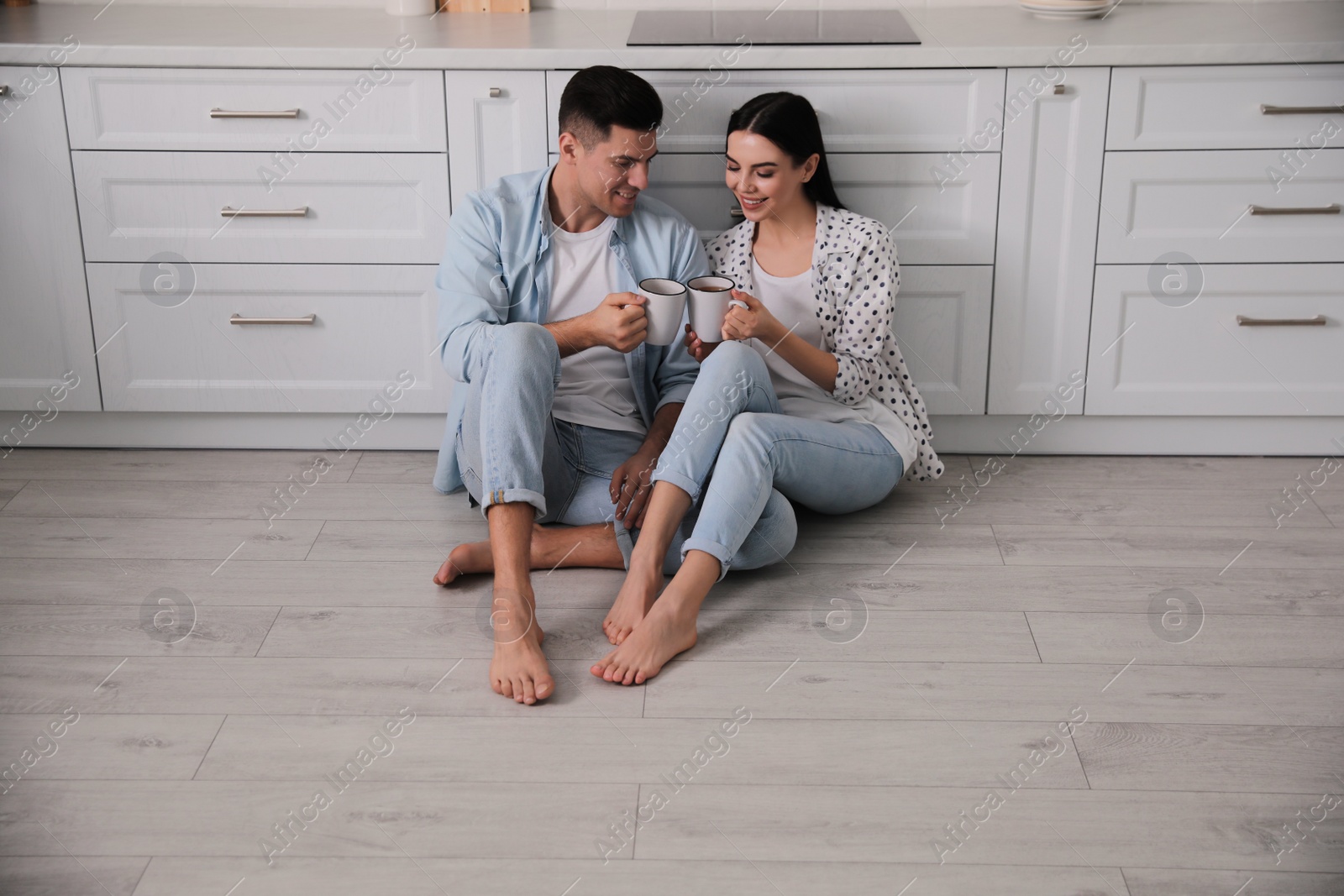 Photo of Happy couple sitting on warm floor in kitchen. Heating system